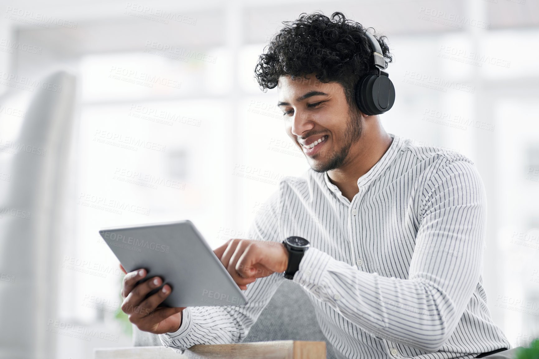 Buy stock photo Shot of a young businessman wearing headphones while using a digital tablet in an office