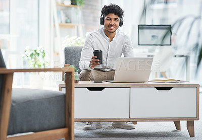 Buy stock photo Shot of a young businessman wearing headphones while working on a laptop in an office