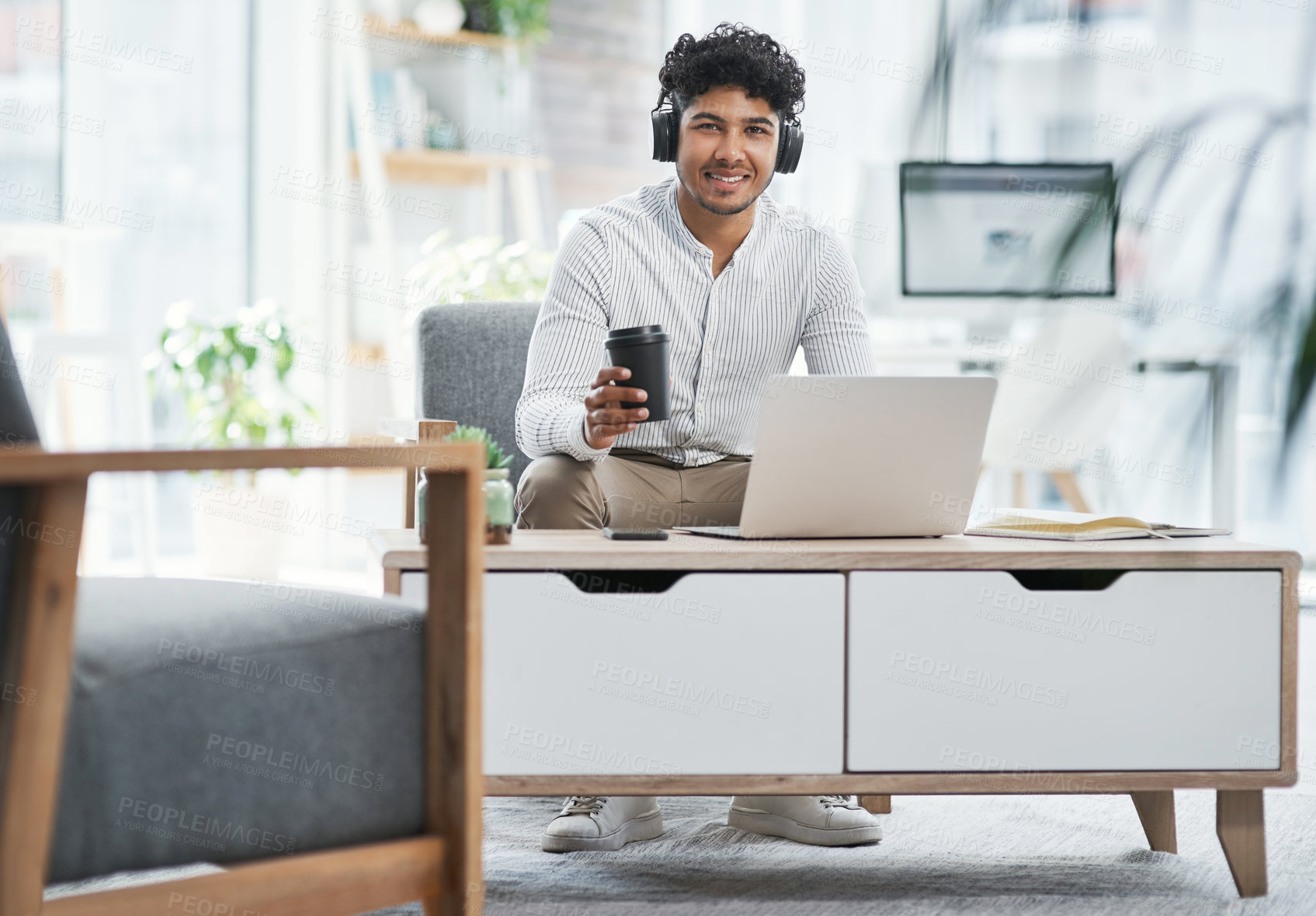 Buy stock photo Shot of a young businessman wearing headphones while working on a laptop in an office