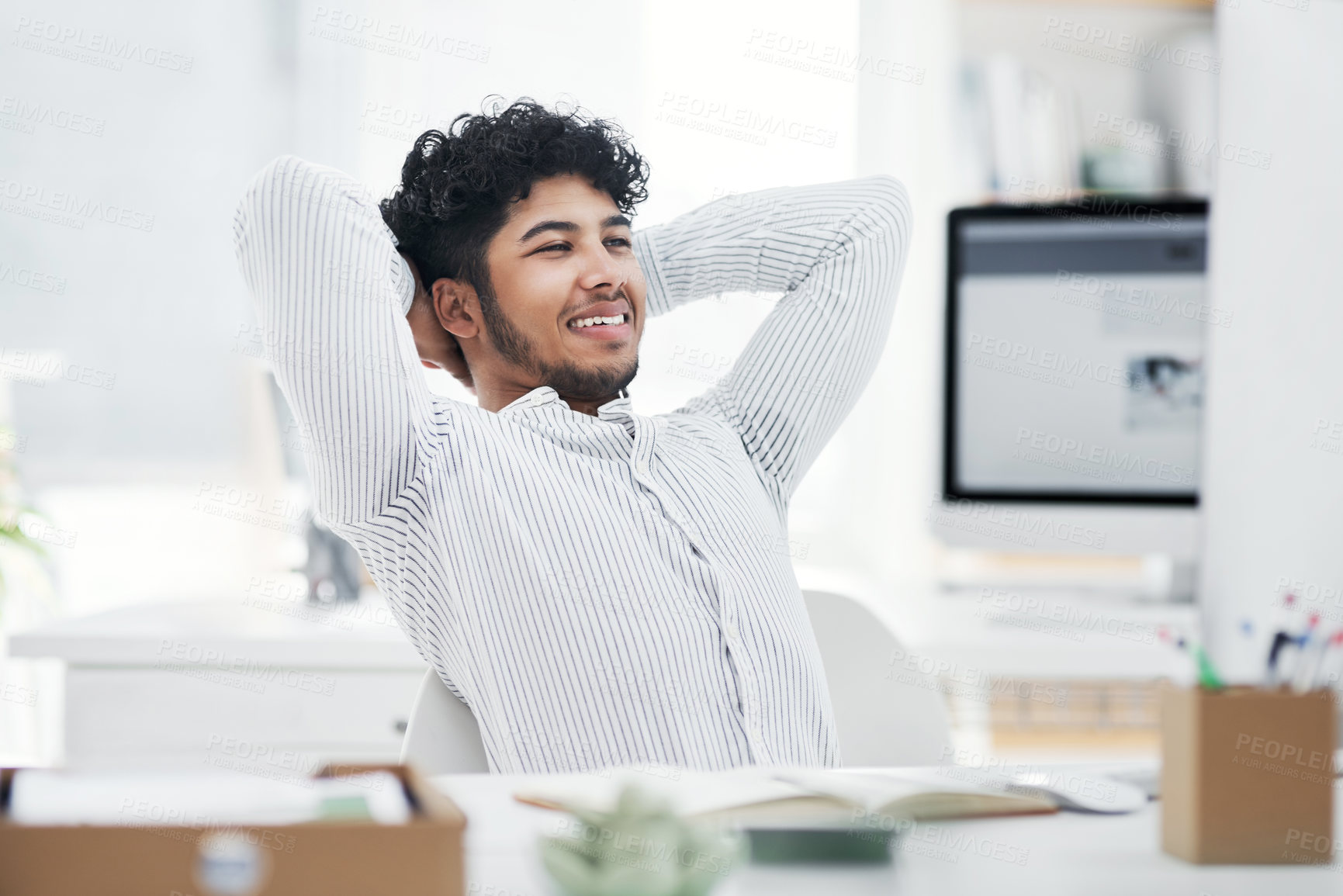 Buy stock photo Shot of a young businessman sitting with his hands behind his head while working in an office