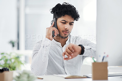 Buy stock photo Shot of a young businessman checking the time on his watch while talking on a cellphone in an office