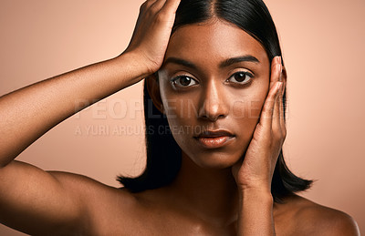 Buy stock photo Portrait of a beautiful young woman touching her face while posing against a brown background