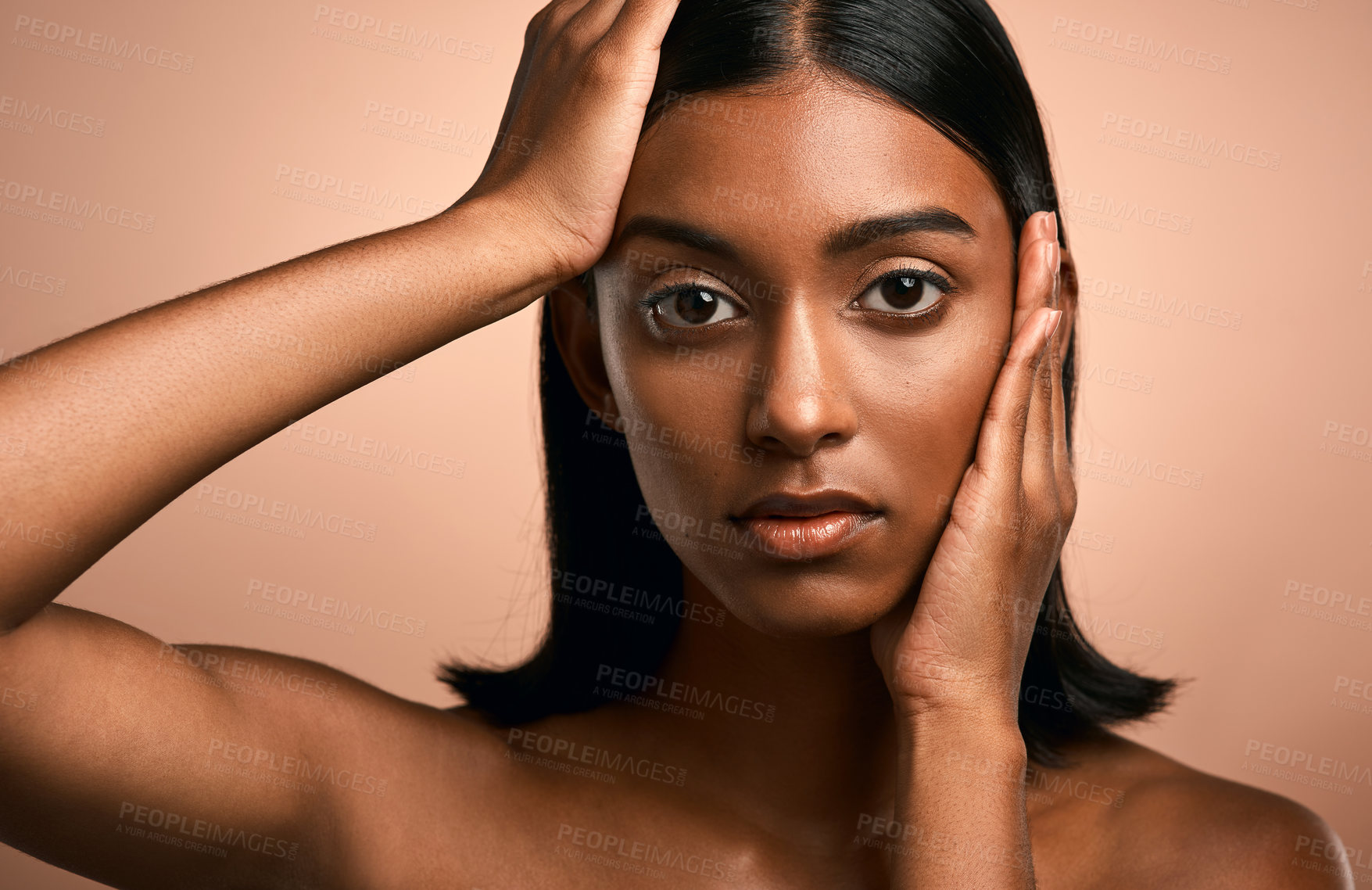 Buy stock photo Portrait of a beautiful young woman touching her face while posing against a brown background