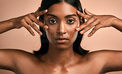 Buy stock photo Portrait of a beautiful young woman touching her face while posing against a brown background