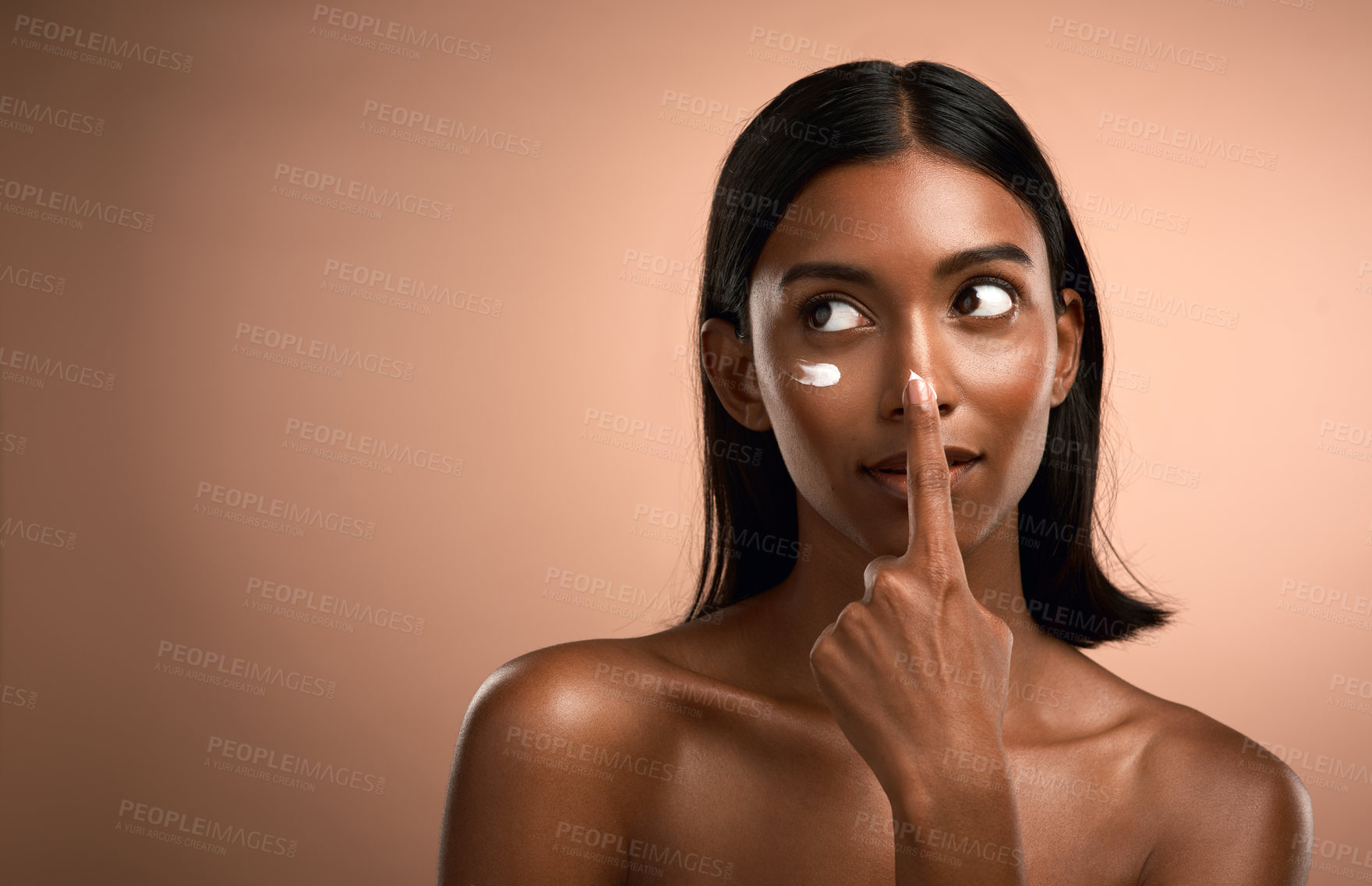 Buy stock photo Shot of an attractive young woman applying moisturiser against a brown background