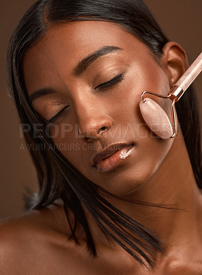 Buy stock photo Closeup shot of an attractive young woman using a derma roller against a brown background