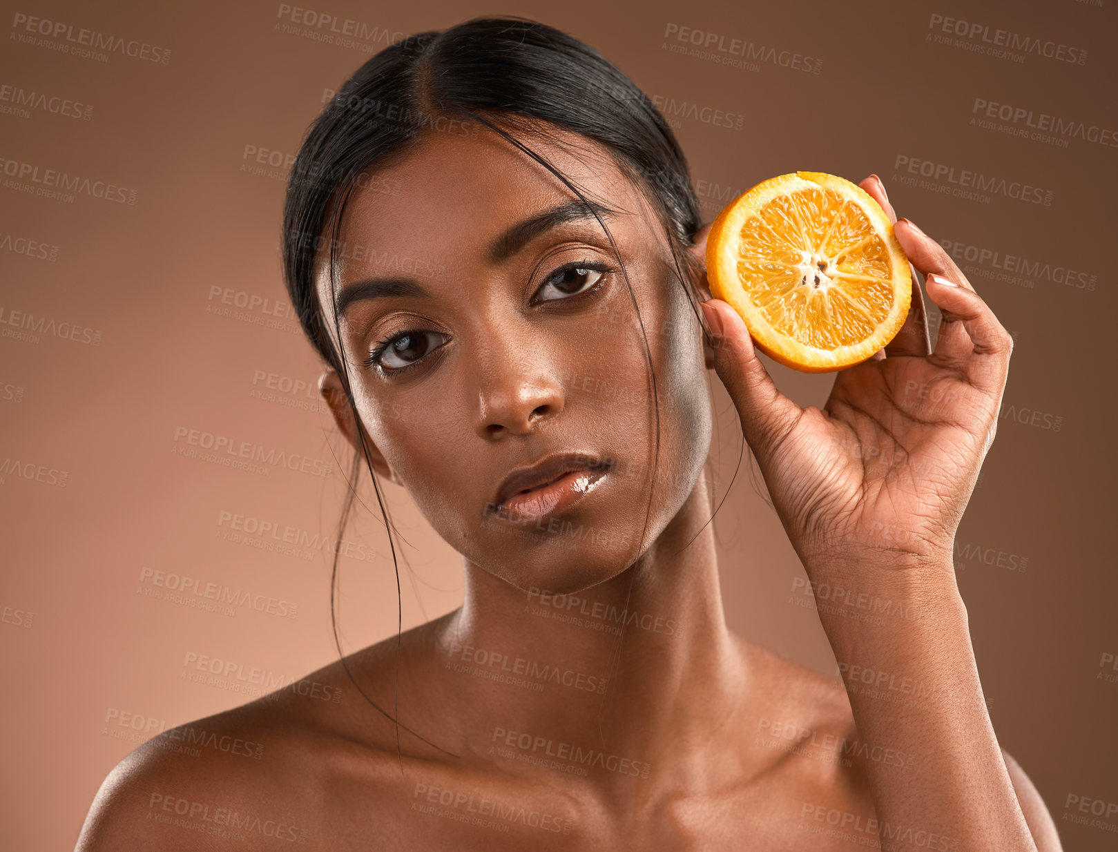 Buy stock photo Portrait of a beautiful young woman posing with an orange against a brown background