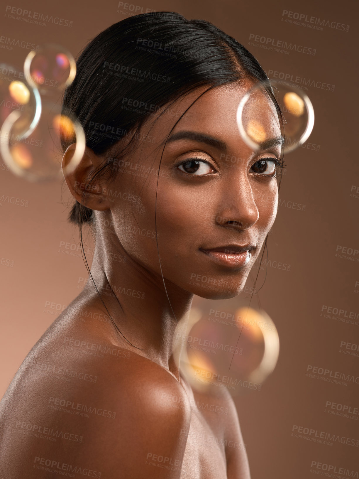 Buy stock photo Portrait of a young attractive woman posing with bubbles against a brown background