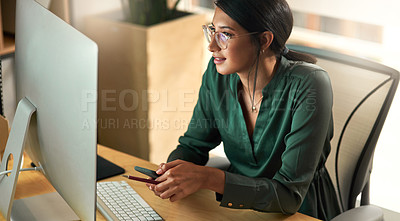 Buy stock photo Shot of a businesswoman using her smartphone while looking at her PC screen