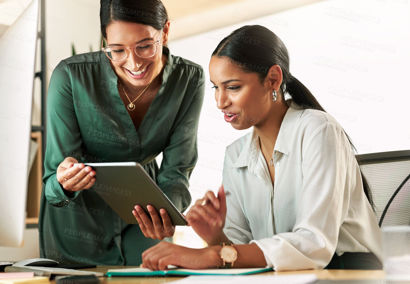 Buy stock photo Shot of two businesswomen using a digital tablet to oversee work