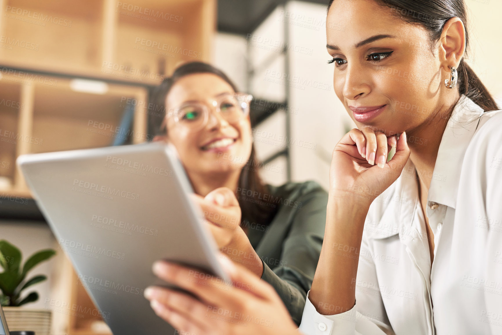 Buy stock photo Shot of two businesswomen using a digital tablet to oversee work