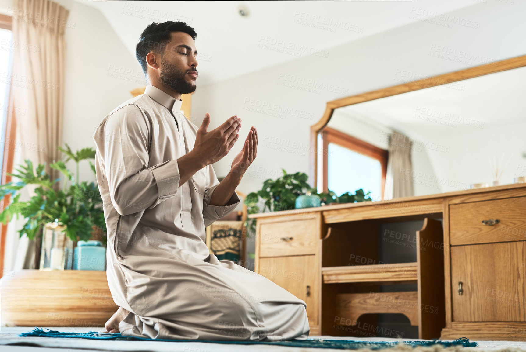 Buy stock photo Shot of a young muslim man praying in the lounge at home