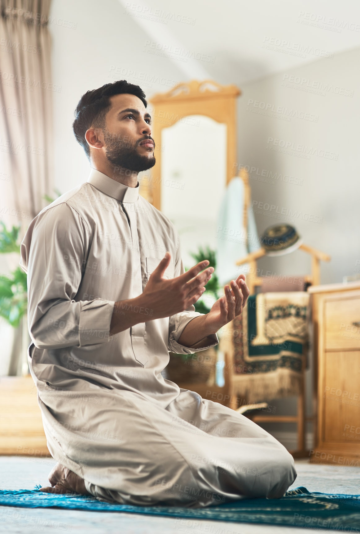 Buy stock photo Shot of a young muslim man praying in the lounge at home