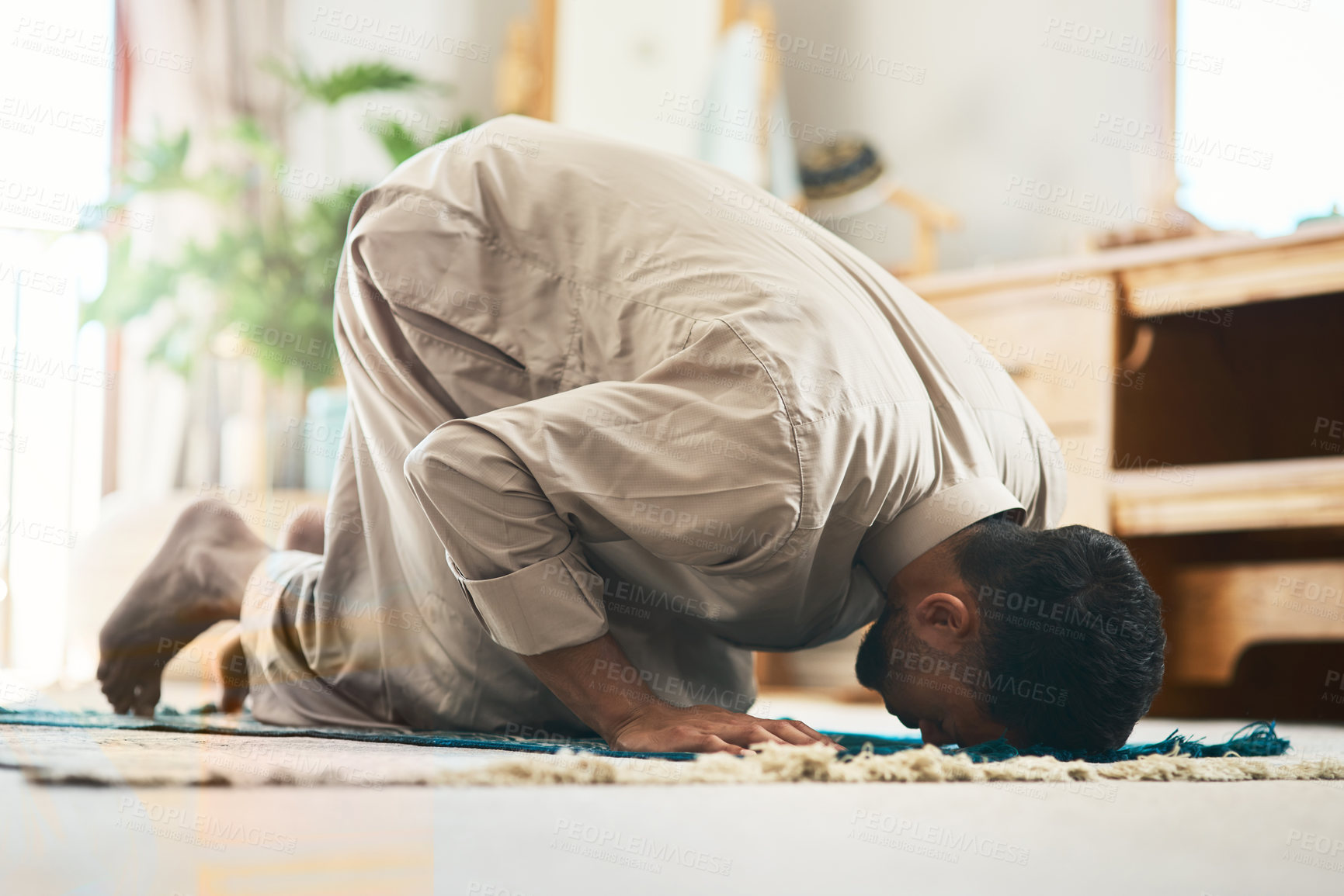 Buy stock photo Shot of a young muslim man praying in the lounge at home