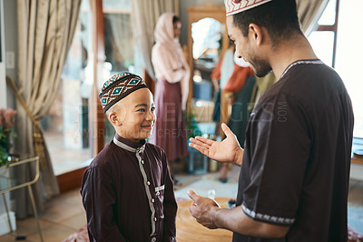 Buy stock photo Muslim father and son talking and bonding in the living room during a religious holiday at home. Cute, smiling and happy Islamic boy listening to advice from his dad while wearing traditional outfit