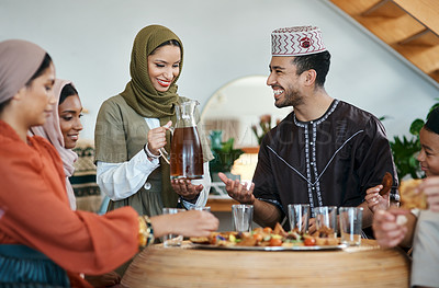 Buy stock photo Group of muslim people celebrating Eid or Ramadan with iftar at home with food, drink and family. Young Islam woman pouring juice for a happy, smiling and positive man while breaking fast together

