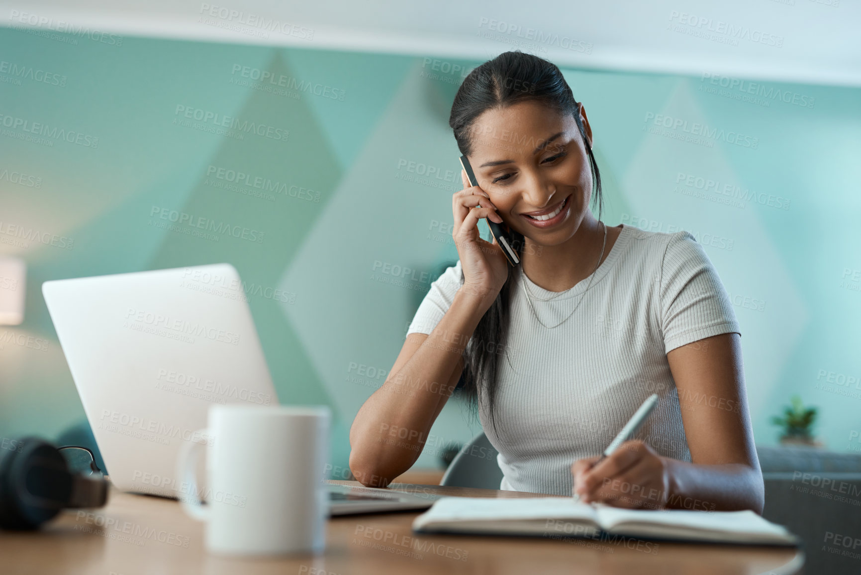 Buy stock photo Shot of a young woman writing in a notebook while on a call at home