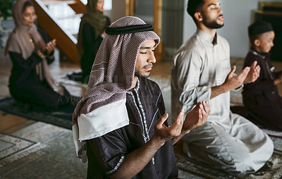 Buy stock photo Young muslim family pray together, sit on knees at home practicing Islam. Religious women wearing hijab and spiritual men wear traditional attire, close eyes and concentrate on prayer with hands up.