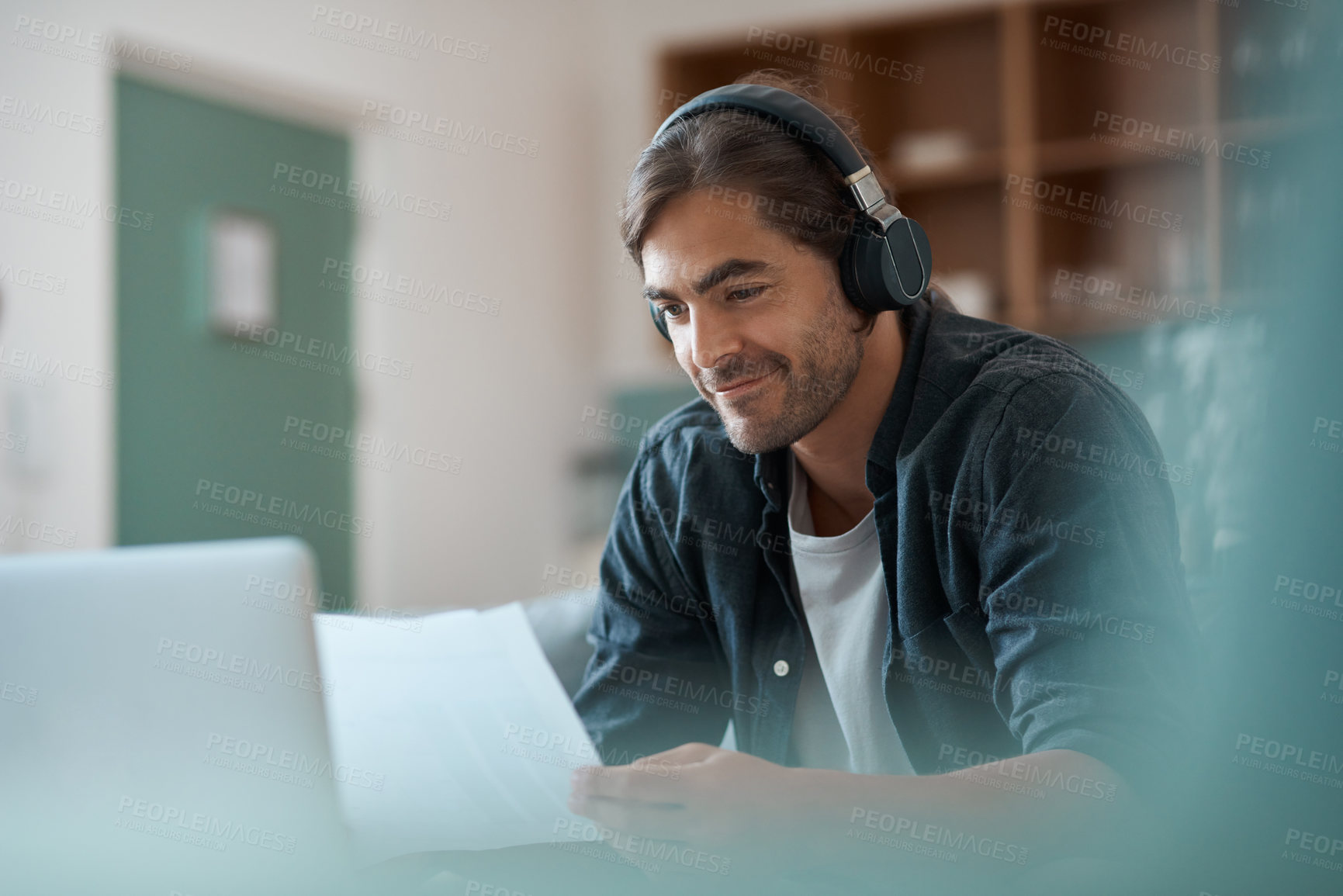 Buy stock photo Shot of a young man doing paperwork while using a laptop at home