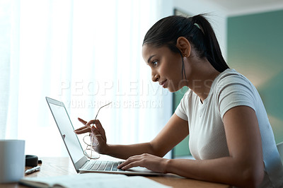 Buy stock photo Shot of a young woman doing paperwork while using a laptop at home
