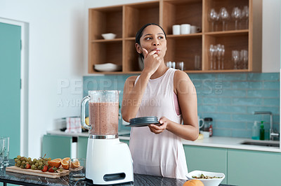 Buy stock photo Cropped shot of an attractive young woman making smoothies in her kitchen at home