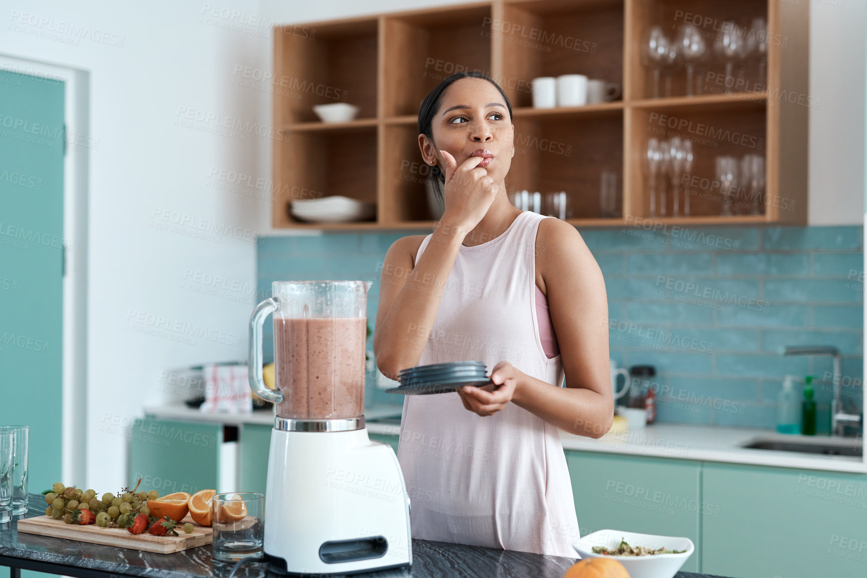 Buy stock photo Cropped shot of an attractive young woman making smoothies in her kitchen at home