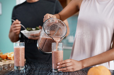 Buy stock photo Cropped shot of an unrecognizable and affectionate young couple making smoothies in their kitchen at home