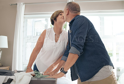 Buy stock photo Shot of a mature couple sharing a kiss while folding their laundry