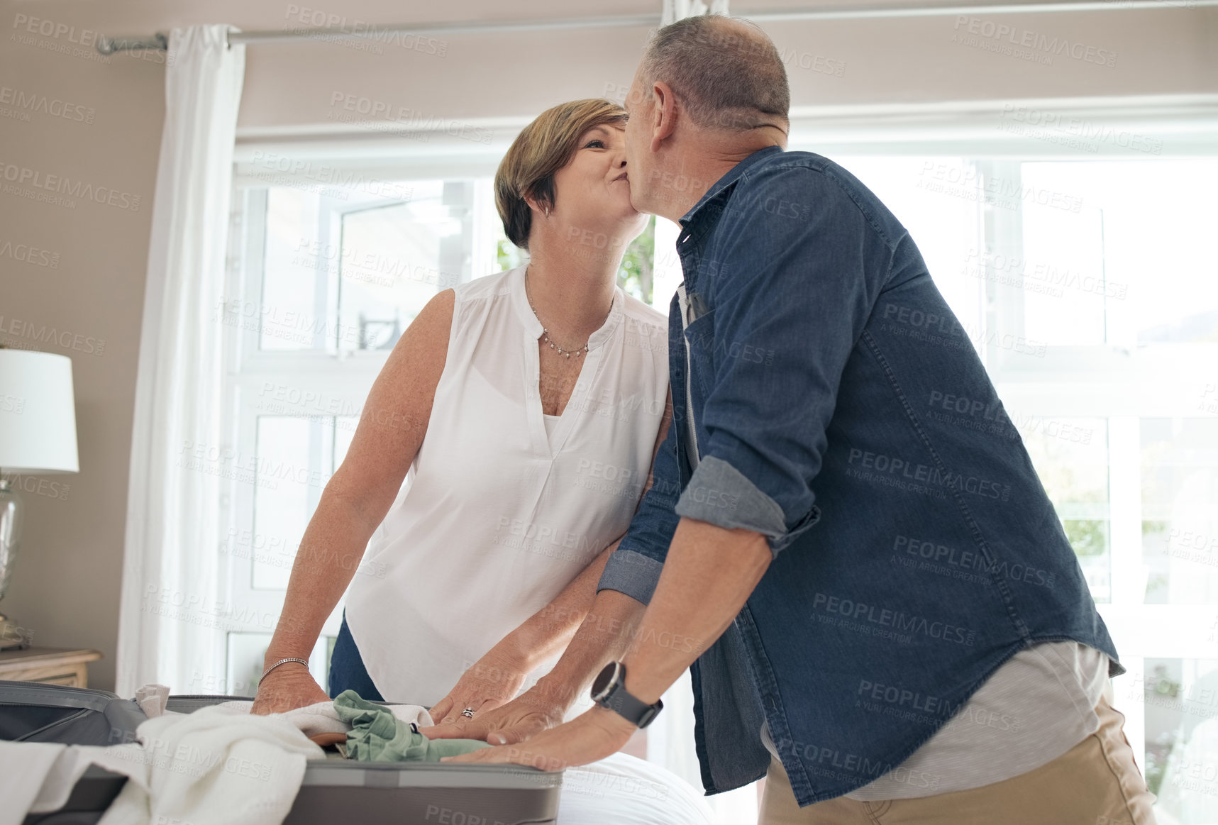 Buy stock photo Shot of a mature couple sharing a kiss while folding their laundry