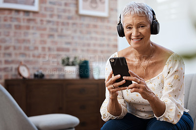 Buy stock photo Shot of a senior woman using a smartphone and headphones on the sofa at home