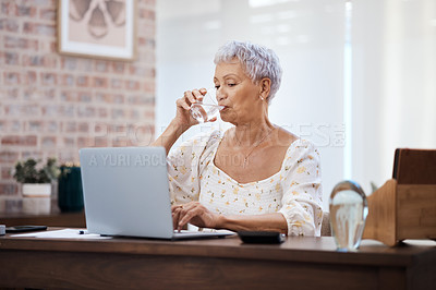 Buy stock photo Shot of a senior woman using a laptop and drinking water at home