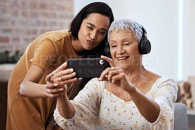 Buy stock photo Shot of a senior woman using a smartphone to take selfies with her daughter at home
