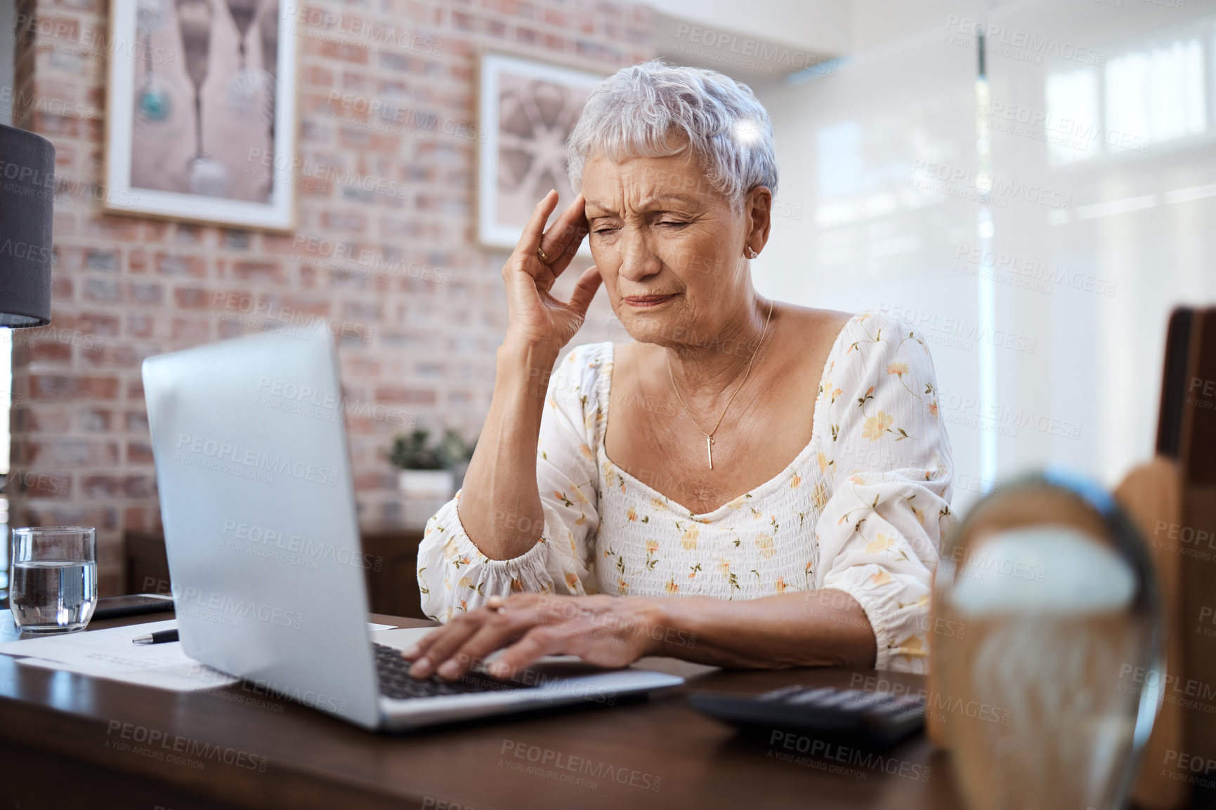 Buy stock photo Shot of a senior woman looking stressed while using a laptop at home