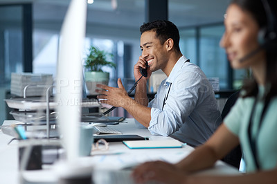 Buy stock photo Shot of a young man answering the phone while working in a modern call centre