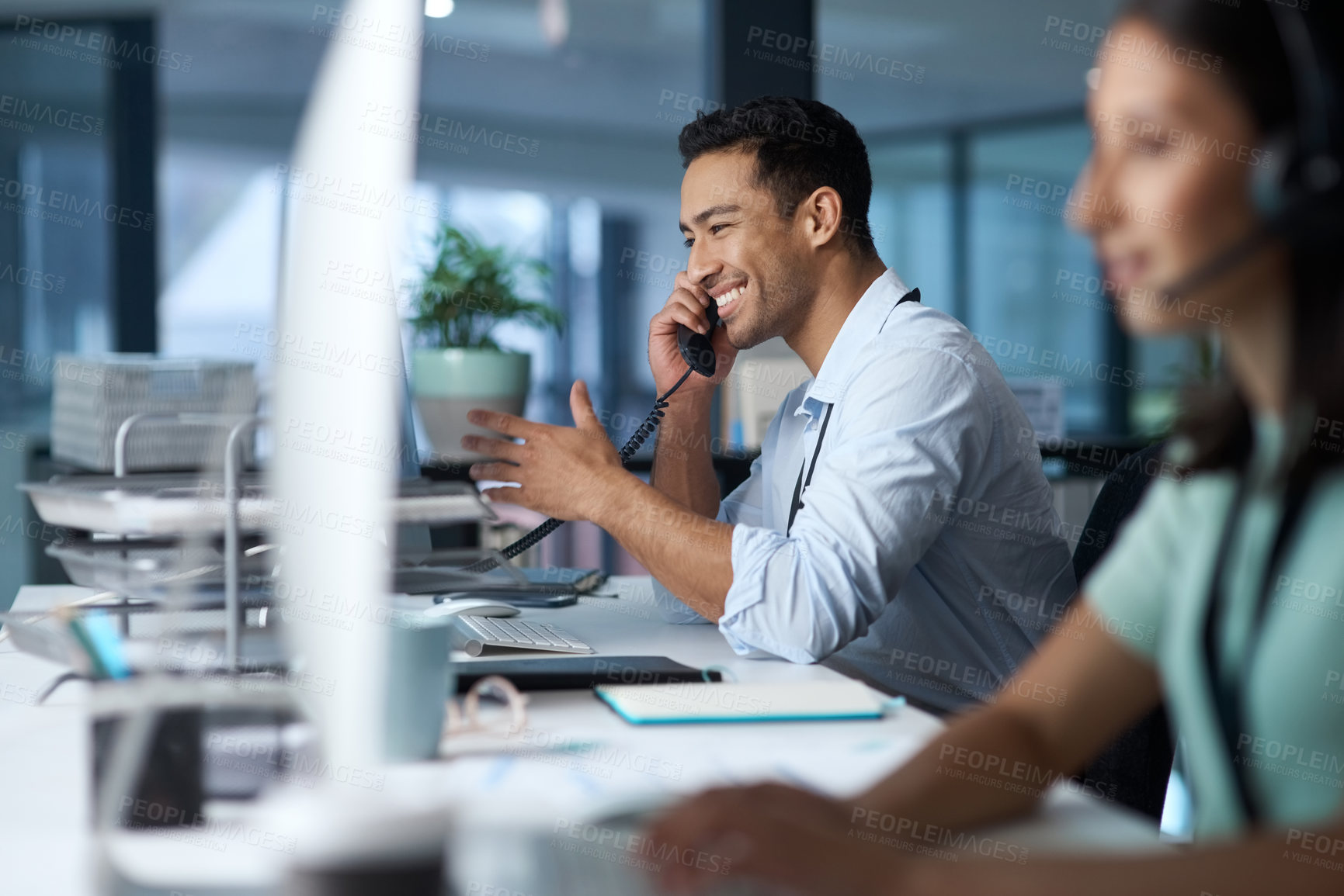 Buy stock photo Shot of a young man answering the phone while working in a modern call centre