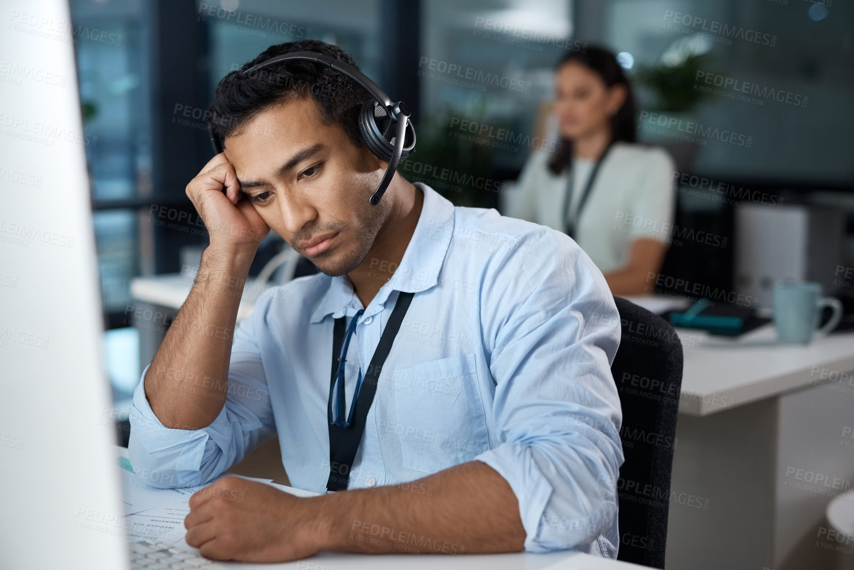 Buy stock photo Shot of a young man using a headset and looking depressed in a modern office