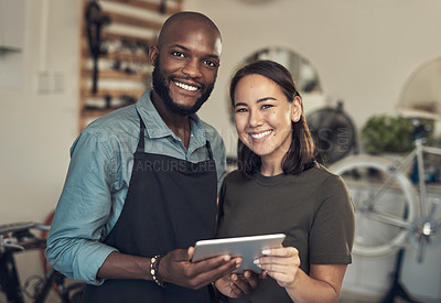 Buy stock photo Shot of two young business owners standing together in their bicycle shop and using a digital tablet