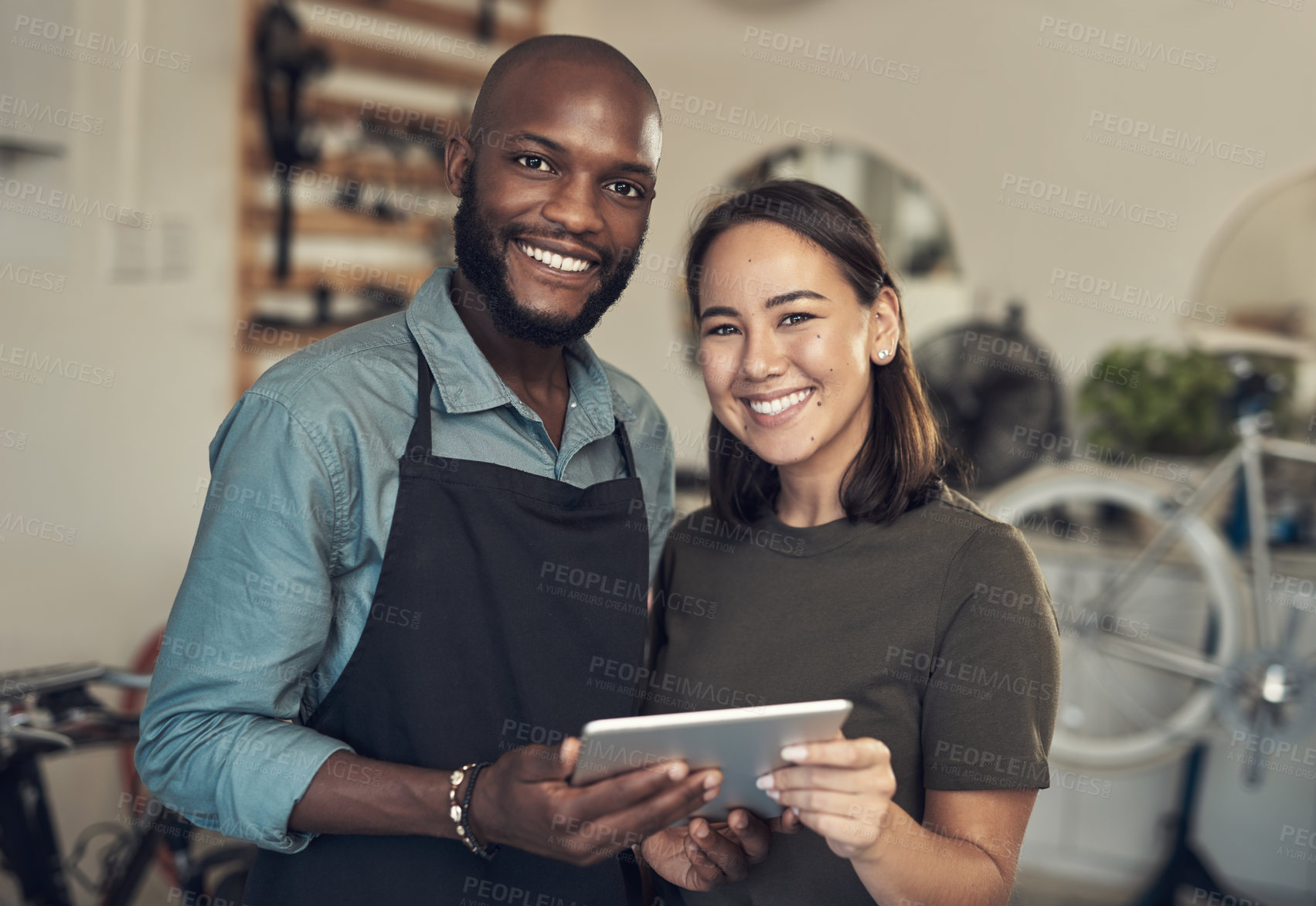 Buy stock photo Shot of two young business owners standing together in their bicycle shop and using a digital tablet