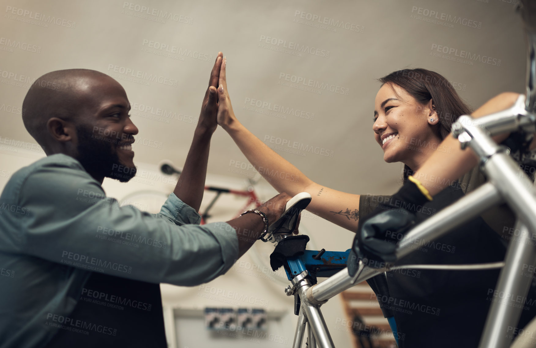 Buy stock photo Shot of two young business owners standing together in their bicycle shop and giving each other a high five