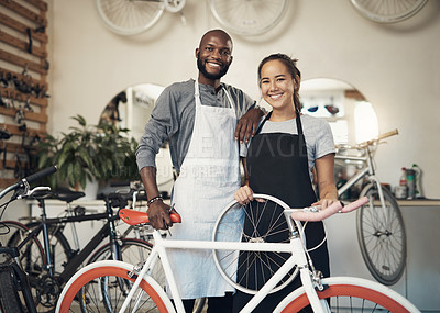 Buy stock photo Portrait of two young workers holding a bike at a bicycle repair shop