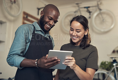 Buy stock photo Shot of two young colleagues standing together in their bicycle shop and using a digital tablet