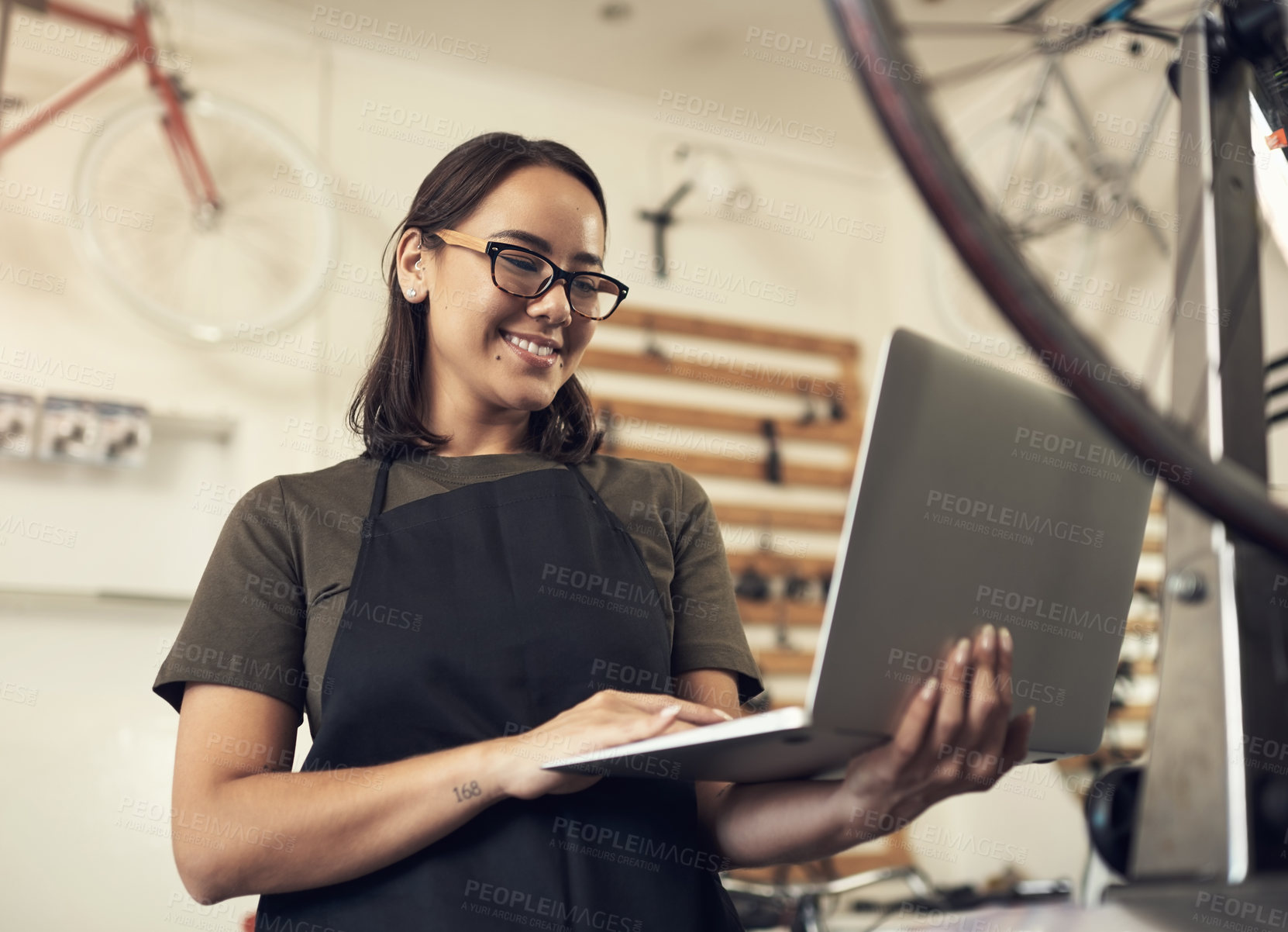 Buy stock photo Shot of an attractive young woman standing alone in her bicycle shop and using her laptop