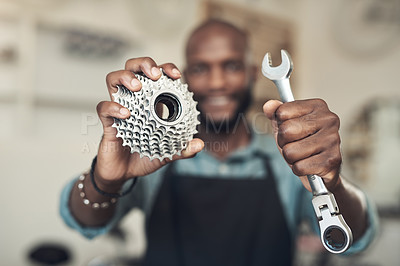 Buy stock photo Shot of an unrecognizable man standing alone in his bicycle shop while holding a spanner and bicycle cassette