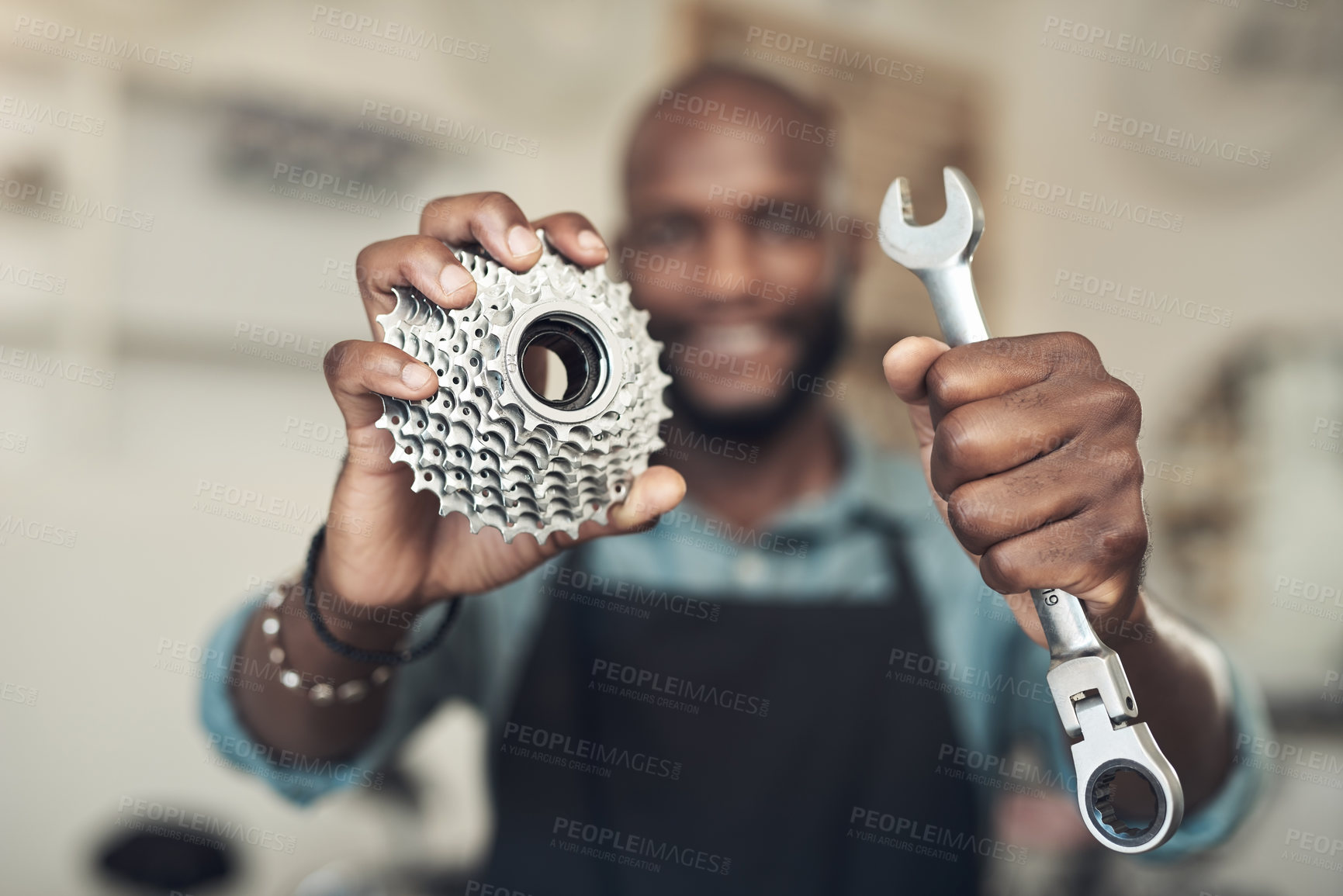 Buy stock photo Shot of an unrecognizable man standing alone in his bicycle shop while holding a spanner and bicycle cassette