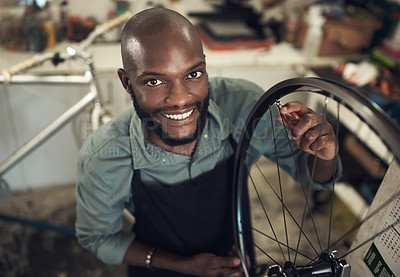 Buy stock photo High angle shot of a handsome young man standing alone in his shop and repairing a bicycle wheel