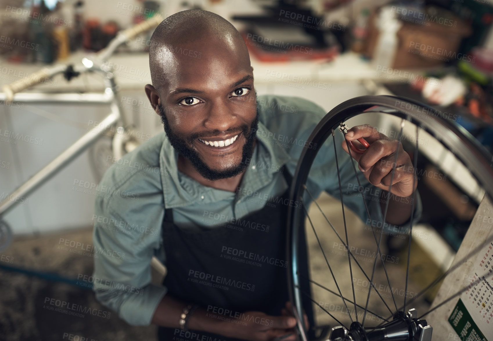 Buy stock photo High angle shot of a handsome young man standing alone in his shop and repairing a bicycle wheel