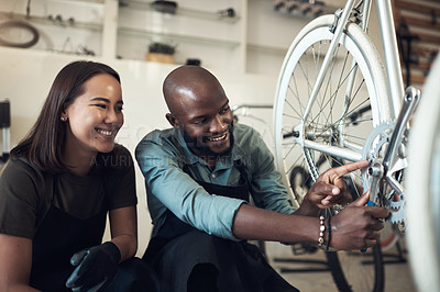 Buy stock photo Shot of two young business owners crouching in their shop and fixing a bicycle wheel