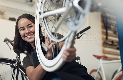 Buy stock photo Shot of an attractive young woman crouching alone in her shop and repairing a bicycle wheel