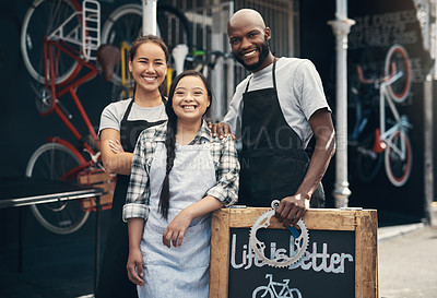 Buy stock photo Portrait of three young working workers standing behind a bicycle repair sign outside