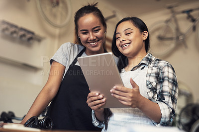 Buy stock photo Shot of two young women using a digital tablet at work